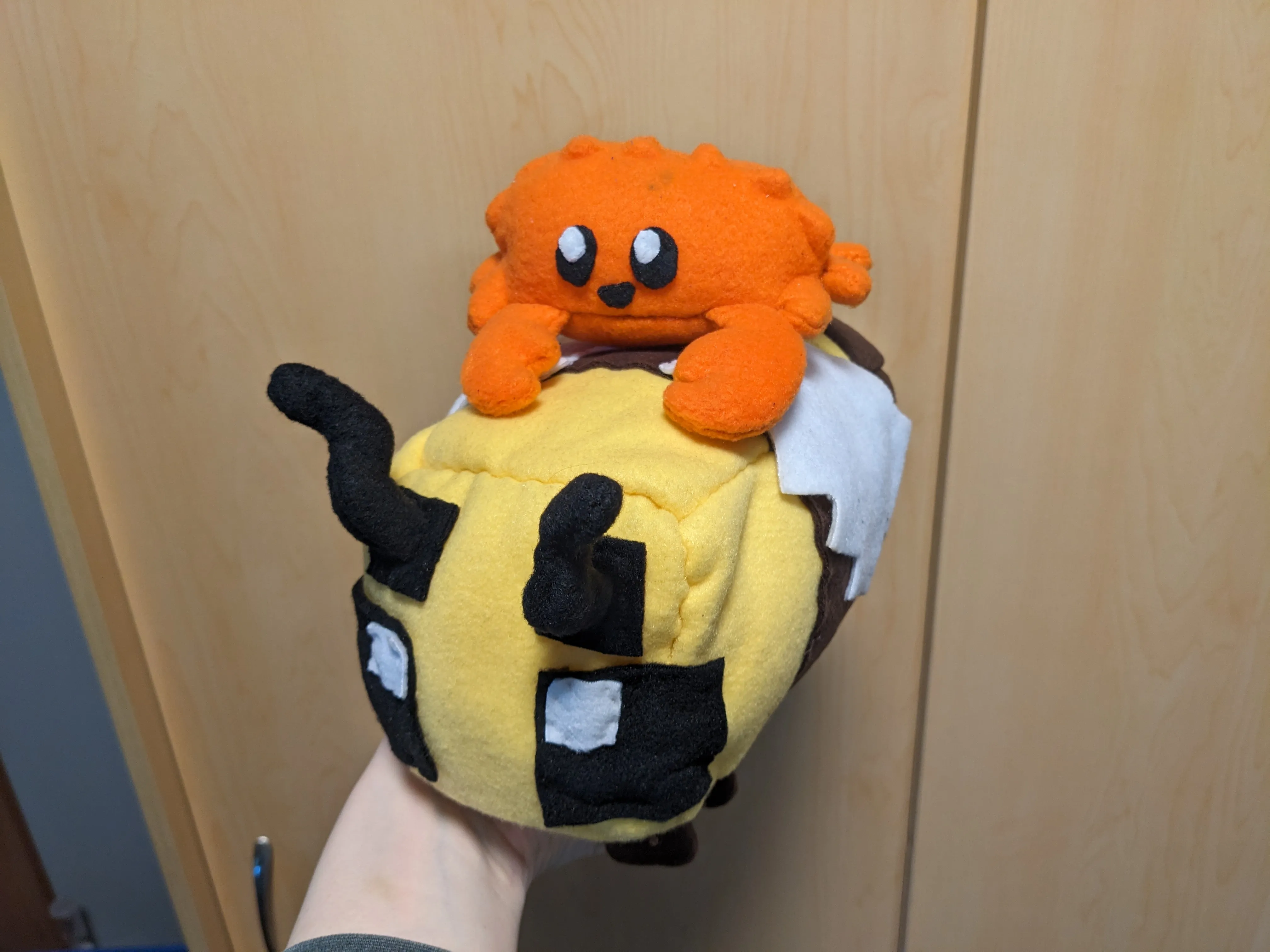 my hand holding my pushie minecraft bee but also there is my plushie ferris crab on top of the bee